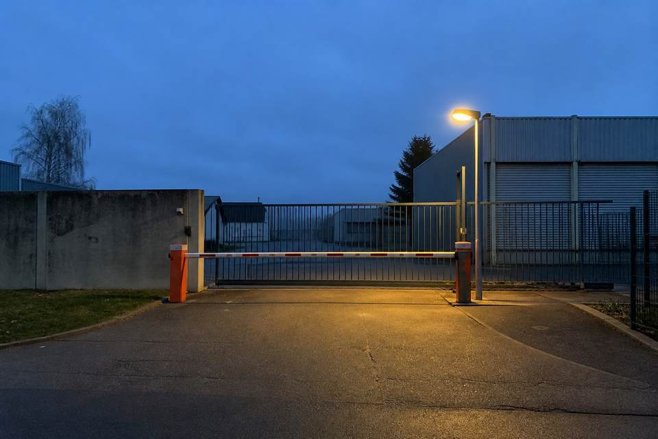 Illustration de synthèse : entrée générique d'un site professionnel fermée par un portail et une barrière à la tombée du jour.