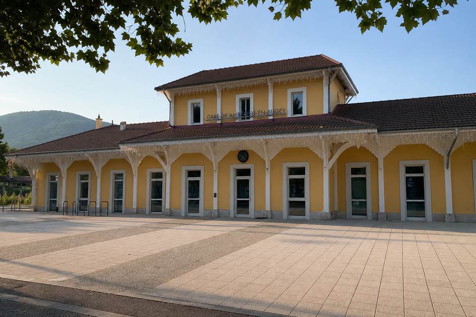 Illustration territoriale de synthèse : façade et parvis de la gare d'Ambérieu-en-Bugey, devant les reliefs du Bugey.